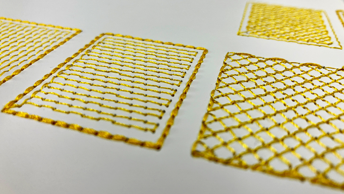 Close up of stitched pattern swatches in gold thread on white paper